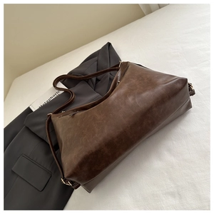 Détail du grand sac cabas marron vintage avec boucle dorée sur un blazer gris foncé