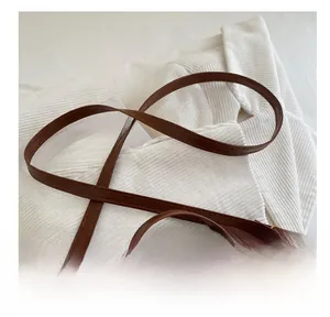 Close-up of brown leather bag strap with gold buckle on a white corduroy background
