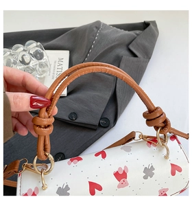 Close-up of heart print cylinder bag with braided handle and gold metal ring details