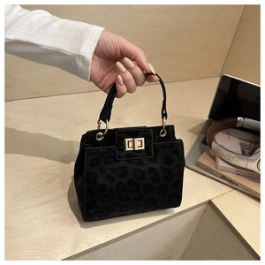 Detail of black leopard embossed handbag with gold turn-lock closure held by hand