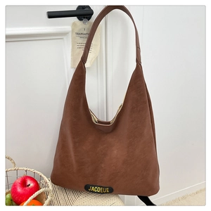 Detail of deep brown Hobo tote bag with a decorative logo label hanging on a door handle