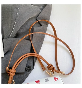 Detail of shoulder bag strap with knotted design, gold metal hooks, and floral heart print