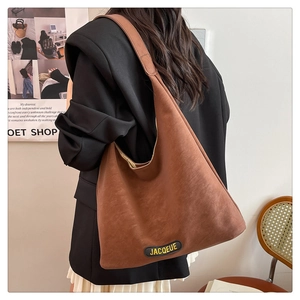 Close-up of wide strap and brand leather tag on dark brown matte faux leather tote bag