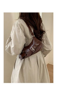 Detail of dark brown glossy leather shoulder bag with buckle strap and bear charm