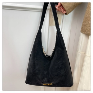 Detail of black matte tote bag with JACQUEUE logo label and minimalist wide shoulder strap
