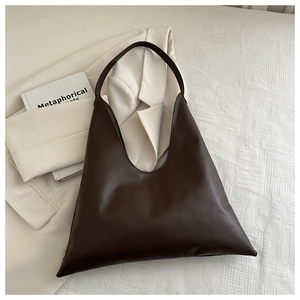 Close-up of minimalist dark brown tote bag with wide shoulder strap on beige surface