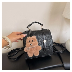 Detail of black faux leather handbag with animal prints and brown plush bear charm