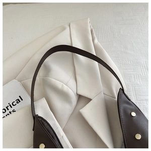 Close-up of brown leather shoulder bag with gold rivets on a white blazer