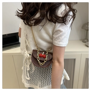 Detail of mini saddle bag in dark brown faux leather featuring cherry decor and gold chains