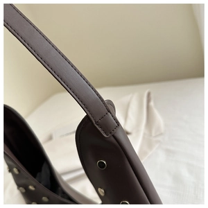 Detailed close-up of dark brown leather shoulder bag with silver studs and stitching