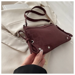 Macro view of burgundy suede shoulder bag featuring metal eyelets and bow tie detail