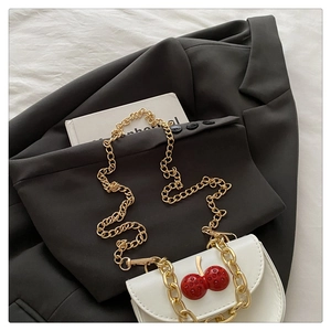 Detail shot of white leather crossbody bag with red cherry charm and gold chain