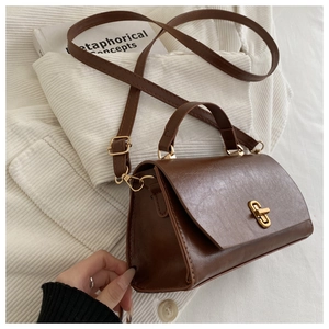 Close-up of vintage brown leather handbag with gold twist lock on a soft knit fabric