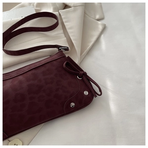 Detail of burgundy leopard print shoulder bag with decorative bow and silver metal rivets