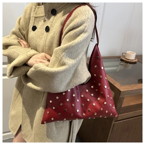 Detail of red leather underarm bag with gold studs on a beige wool coat background