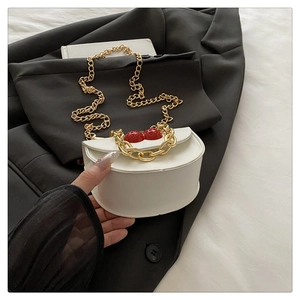 Detail of white semi-circle leather bag featuring red cherry ornaments and gold chains
