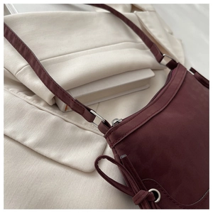 Detail of burgundy suede shoulder bag featuring elegant side drawstring bow and slim strap