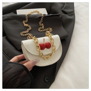 Detail of a white mini saddle bag with red cherry crystal accent and gold chain strap