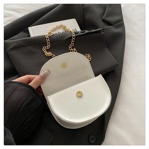 Close-up of white saddle bag with golden chain strap and magnetic snap closure