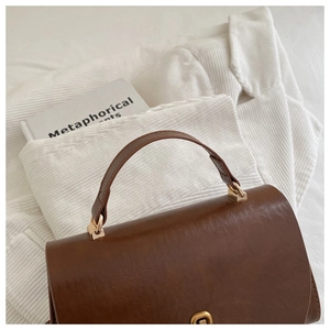 Detail of vintage brown handbag featuring a gold metal clasp and premium leather texture