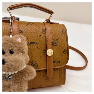 Close-up of brown textured leather bag with cartoon patterns and plush charm detail