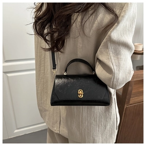 Detail of black glossy leather handbag featuring a gold rectangle twist lock and handle
