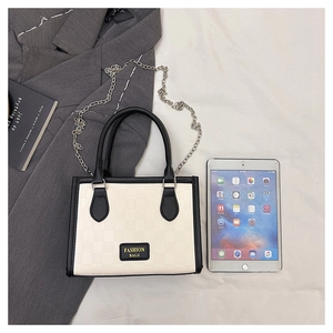 Close-up of cream checkerboard tote bag with black trim and elegant silver chain