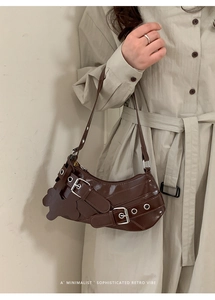 Detail of dark brown patent leather crescent bag with metal buckles and eyelets