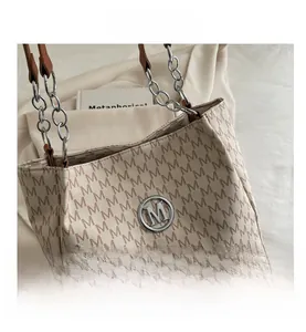 Close-up of vintage tote bag with M print, circular metal logo and chain strap