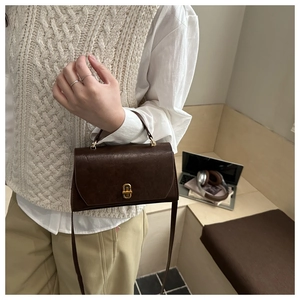 Detail of a vintage dark brown leather handbag featuring a golden turn-lock on a model