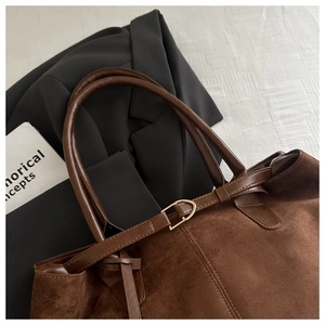 Detail view of brown faux suede tote bag with metal buckle on a white background
