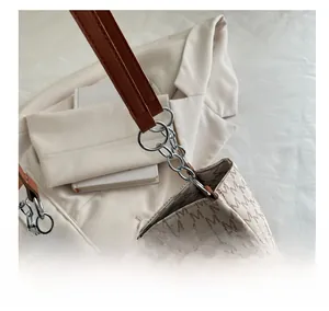 Detail of cream monogram handbag showing silver metal chain link and brown leather strap