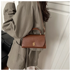 Brown leather crossbody bag with gold buckle styled on an olive green trench coat