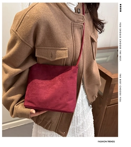 Detail of burgundy velvet bucket bag with embossed text worn over a brown wool coat