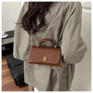 Classic retro brown leather handbag with gold clasp worn by a person over the shoulder