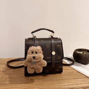 Retro dark brown pebbled leather satchel with rabbit print and plush bear charm on wood