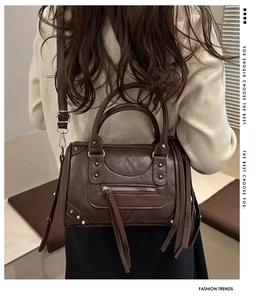 Detail of a brown leather pillow bag featuring metallic rivets and long fringe tassels