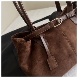 Detail of dark brown suede tote bag with leather straps and gold metal hardware