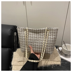 Detail of tweed checkered tote bag with gold chain strap in a cozy coffee shop setting