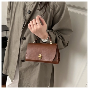 Detail of a brown leather mini flap bag with vintage gold hardware held by a model