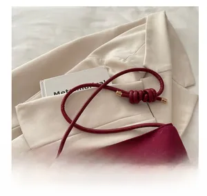 Detail of burgundy suede bucket bag with knotted handle and elegant gold hardware