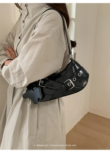 Detail of black glossy underarm bag with silver buckle and bear charm on beige trench coat