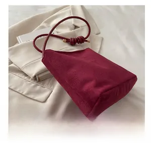 Side view of minimalist burgundy suede bucket bag with knotted shoulder strap and soft texture