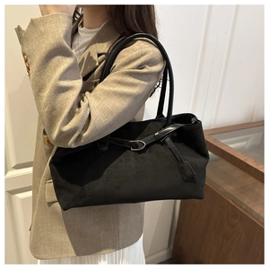Detail of a black suede tote bag with metal buckle strap worn over a khaki blazer