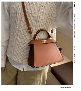 Détail d'un sac à main trapèze en cuir marron avec fermoir doré et côtés en accordéon
