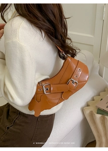 Detail of a brown glossy leather crescent bag with metal eyelets and a bunny charm