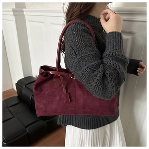 Detail of burgundy faux suede tote bag featuring a square leather tag and slim handles