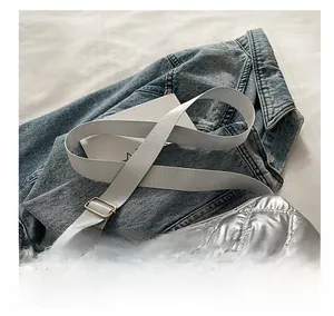 Detail of silver quilted shoulder bag with wide adjustable woven strap on denim
