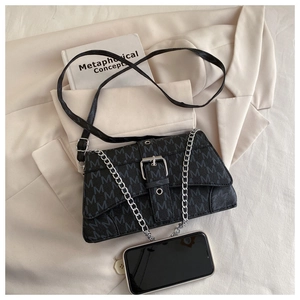Macro shot of dark grey flap bag with M-pattern and chain strap next to a mobile phone