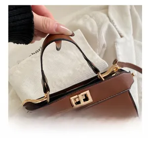 Détail de la poignée du sac en cuir marron avec boucle dorée et finitions de bordures noires